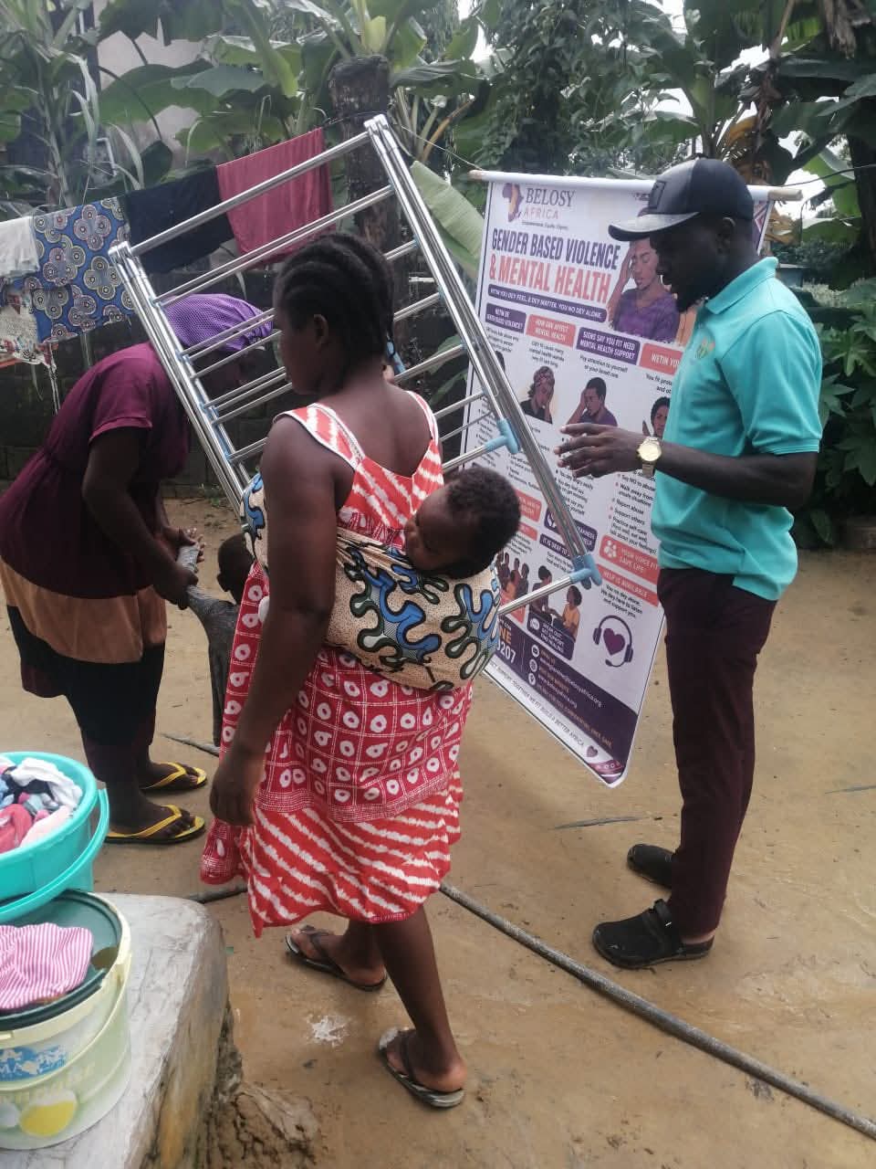 A volunteer explaining the GBV banner to a mother carrying her baby